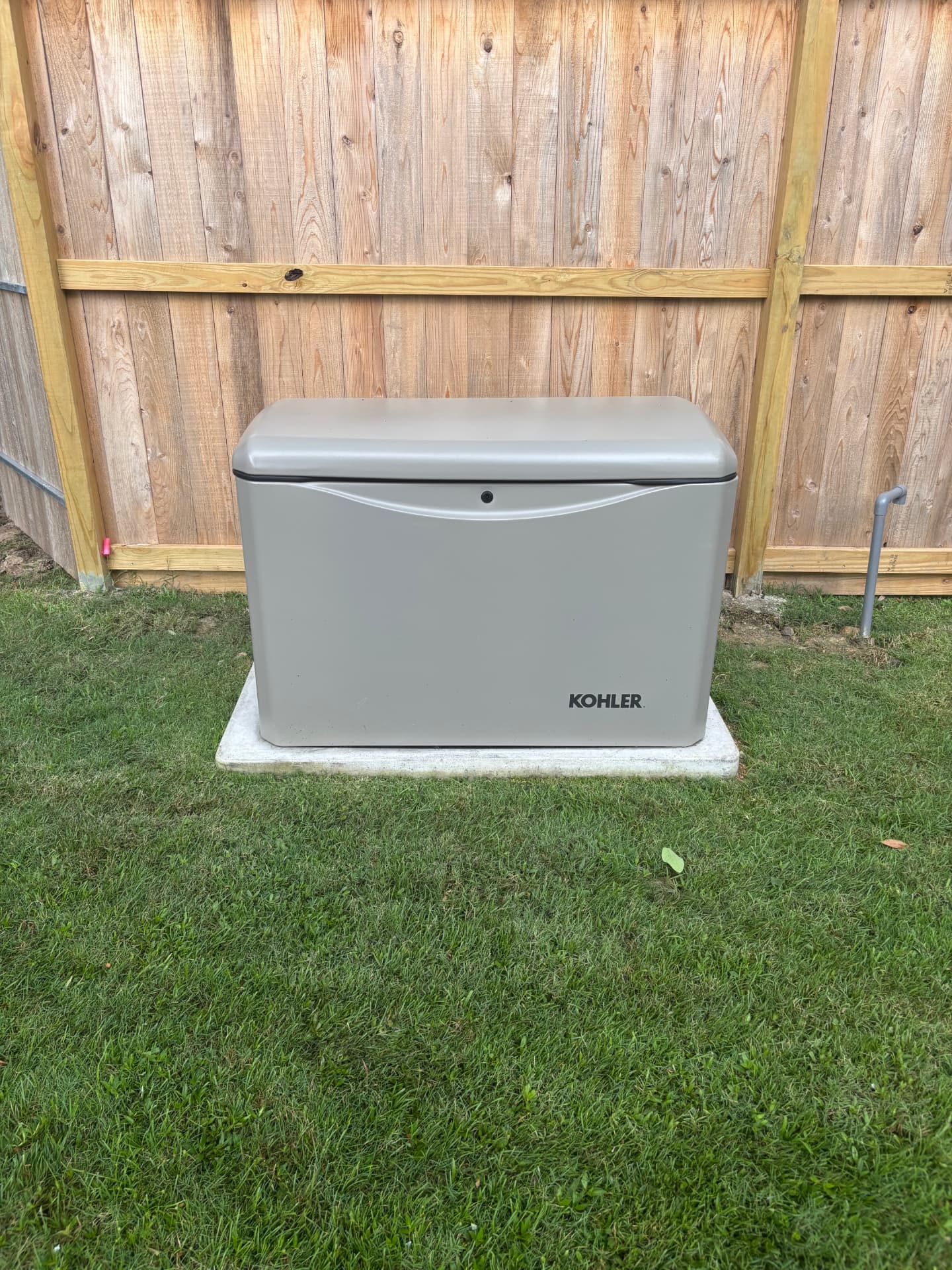 Kohler standby generator installed on a concrete pad beside a wood fence