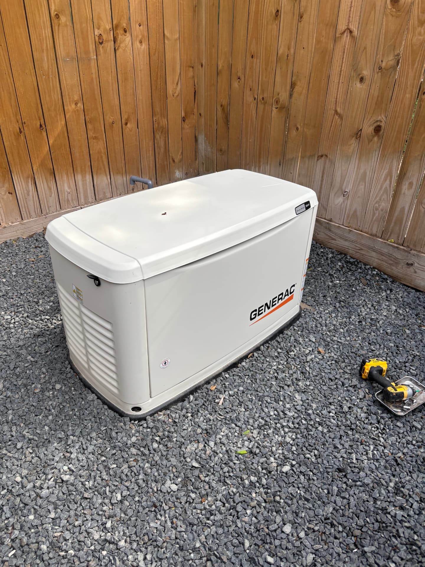Generac standby generator installed on a gravel bed beside a wood fence